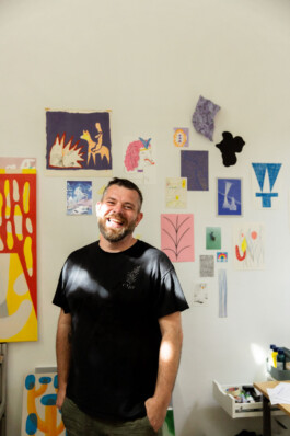 Image of Stef Mosebach in their art studio in front of a wall of drawing and collages.. 